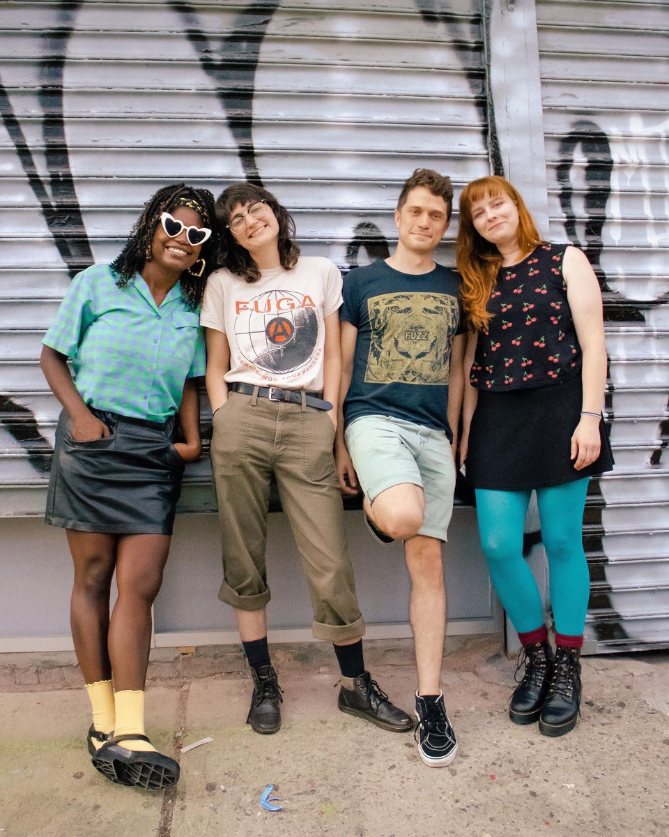 Members of Bacchae standing in front a graffiti-tagged gate